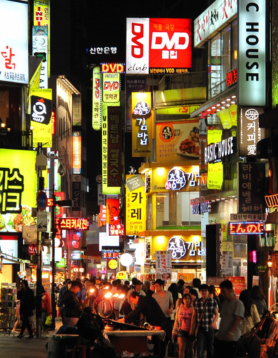 Neon shop and restaurant signs above a crowded Myeongdong street at night