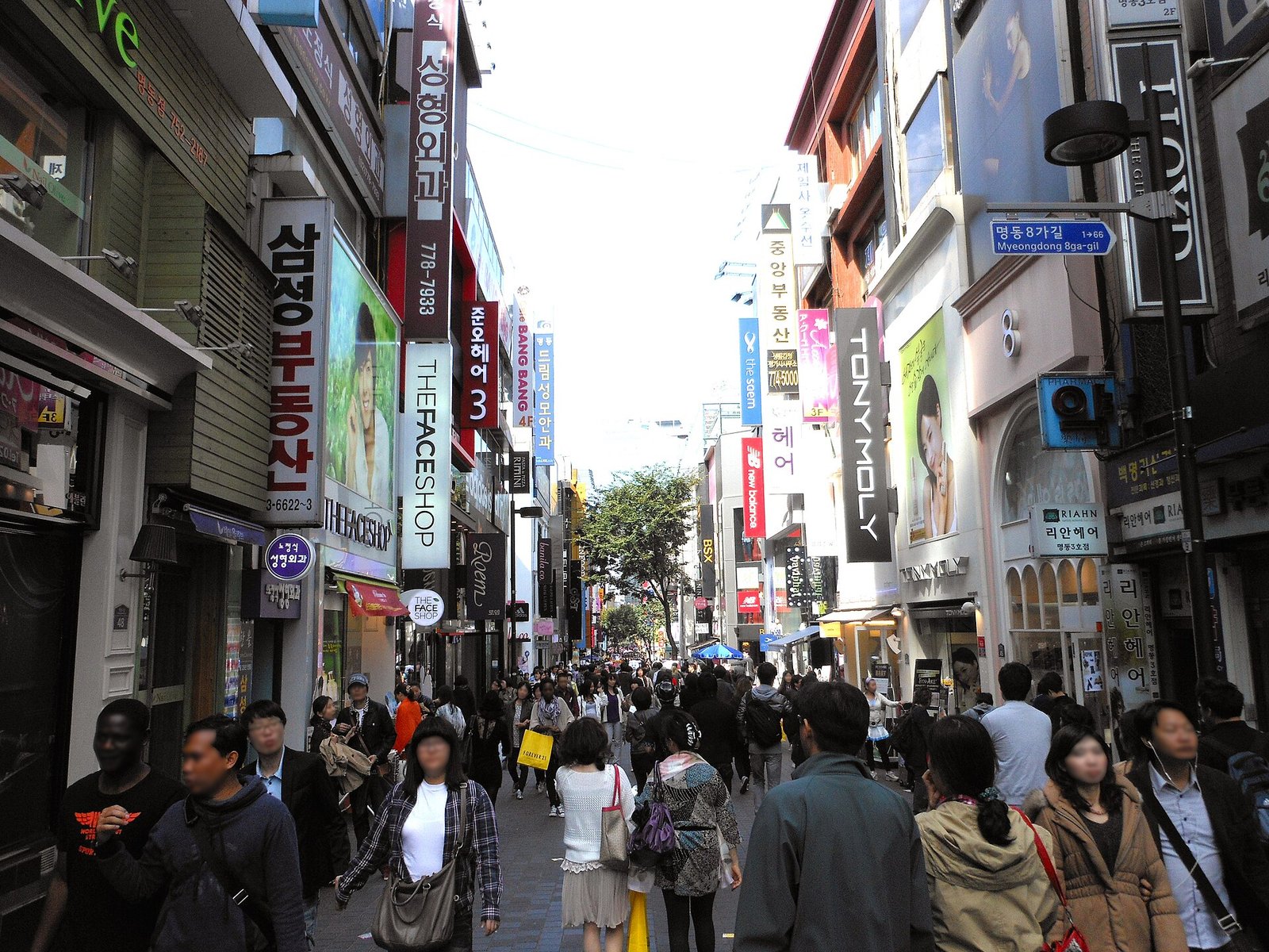 Shoppers walking down a Myeongdong street lined with cosmetics shop signs in daytime