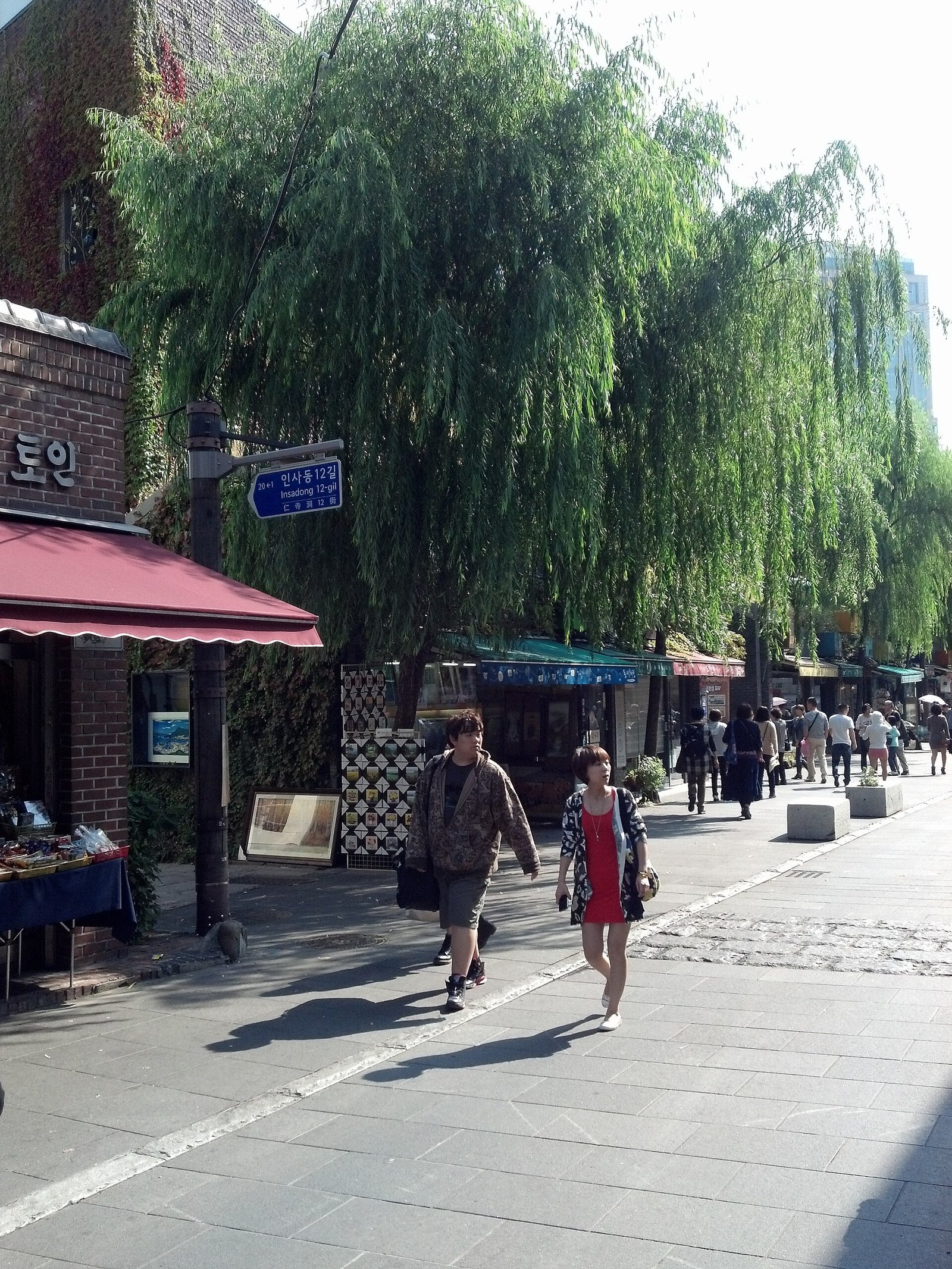 Pedestrians on Insadong-gil in Seoul under willow trees beside small shops