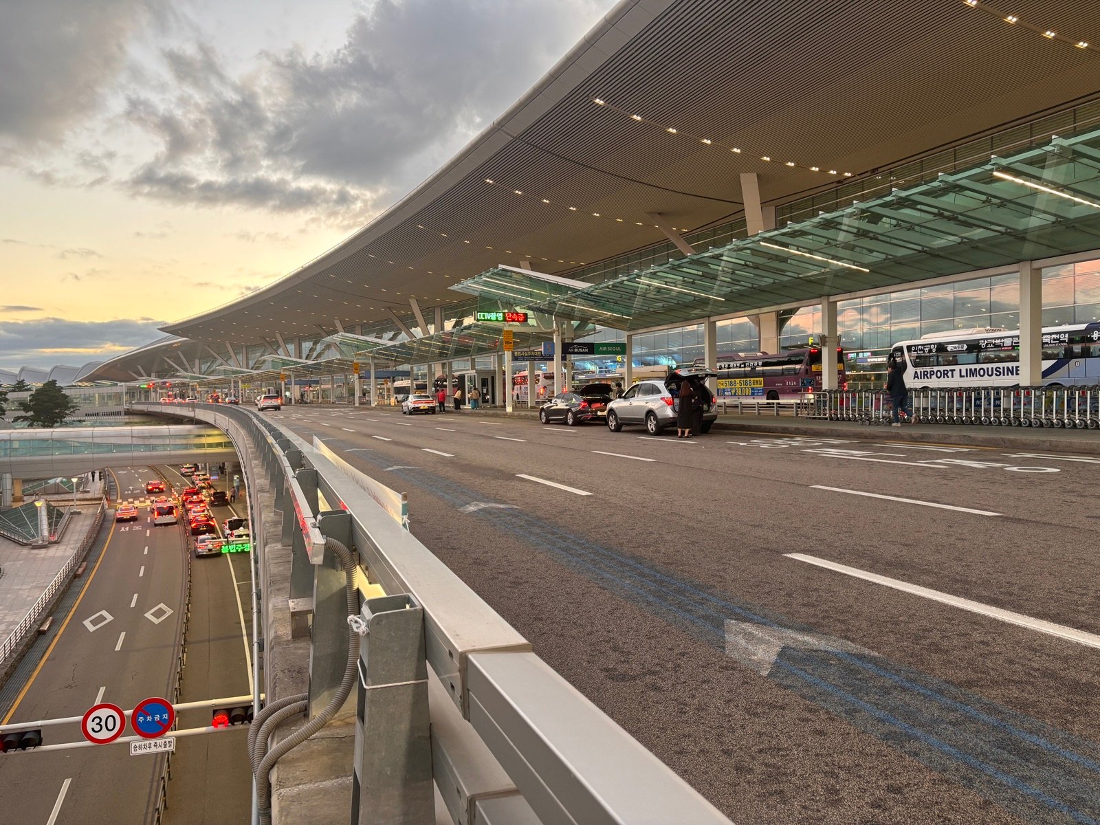 Curbside at Incheon Airport Terminal 2 at dusk, with an Airport Limousine bus and taxis below
