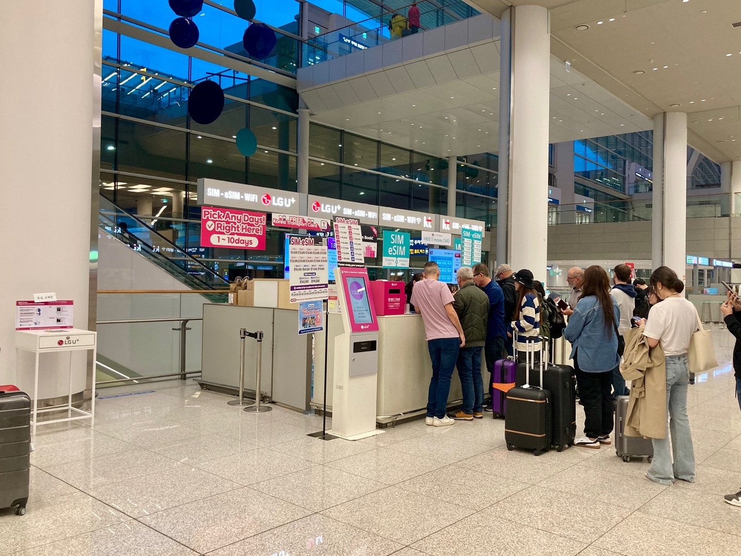Travelers with suitcases lining up at a SIM, eSIM and Wi-Fi counter at Incheon Airport