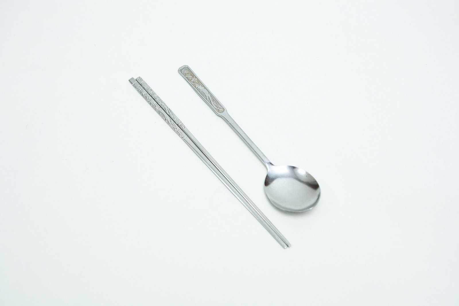 A Korean metal spoon and a pair of metal chopsticks side by side on white