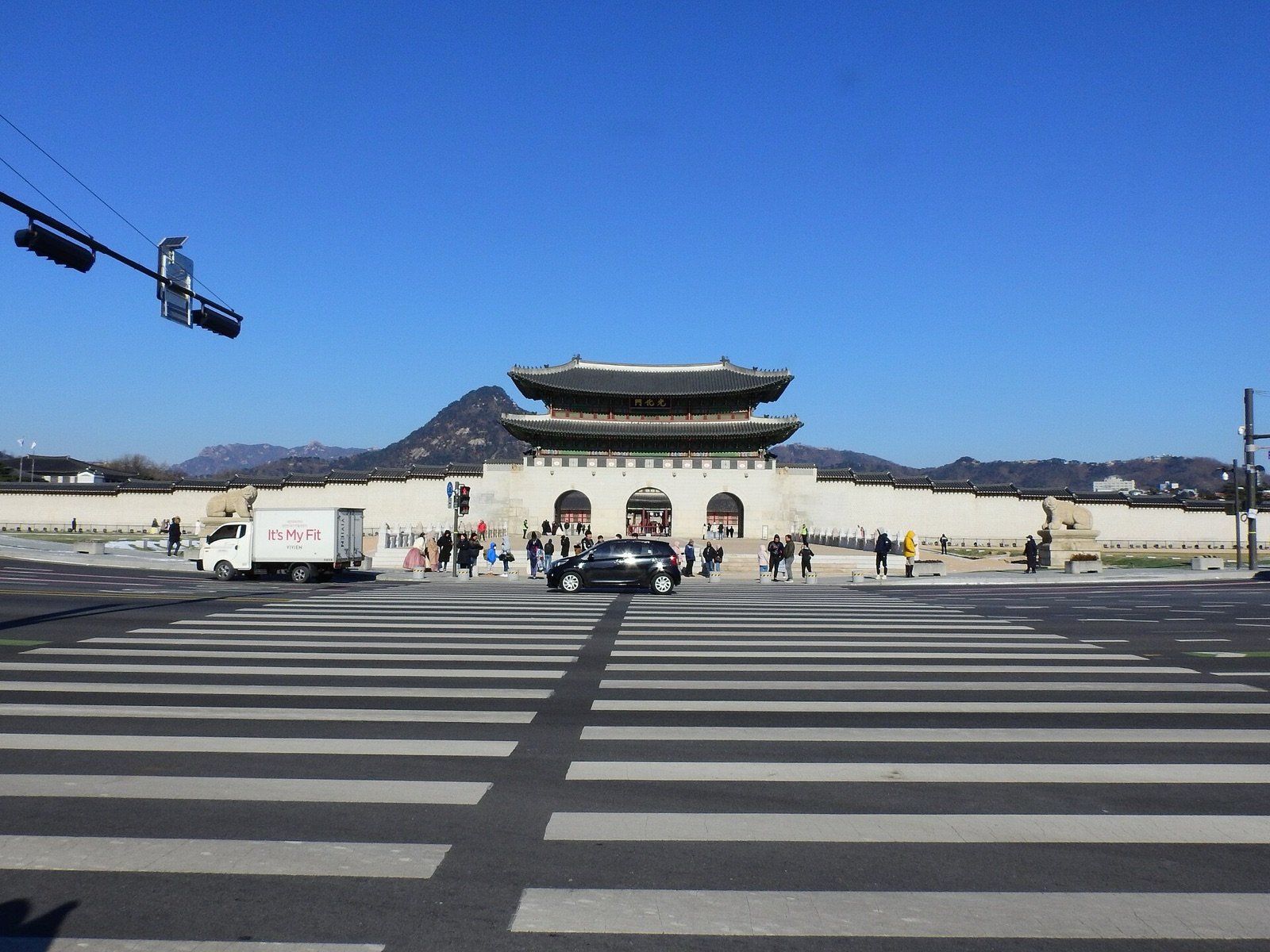 Gwanghwamun gate of Gyeongbokgung Palace beyond a wide crosswalk under a clear blue sky