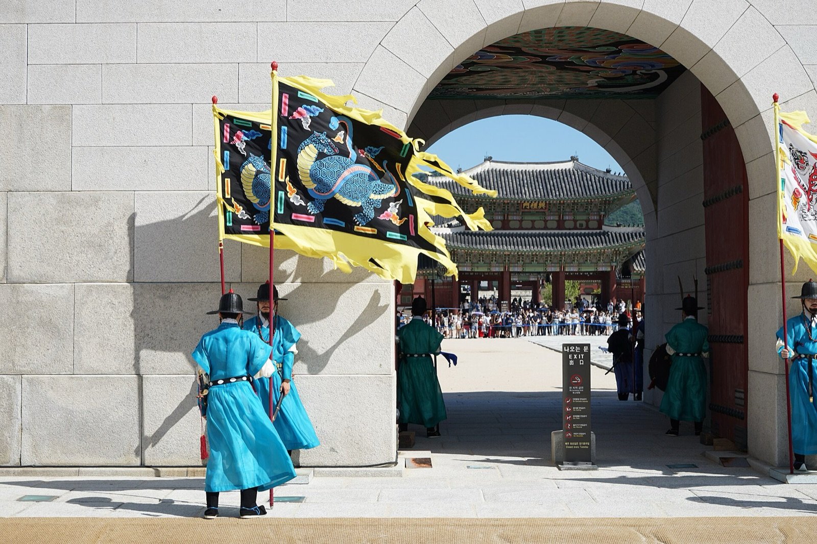 Palace guards in blue and green uniforms with flags at a stone gate of Gyeongbokgung