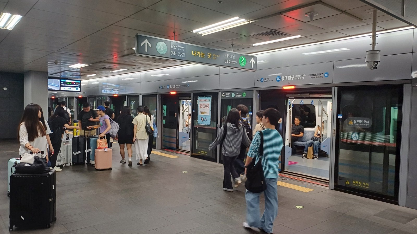 Travelers with suitcases on the Airport Railroad platform at Hongik Univ. Station in Seoul