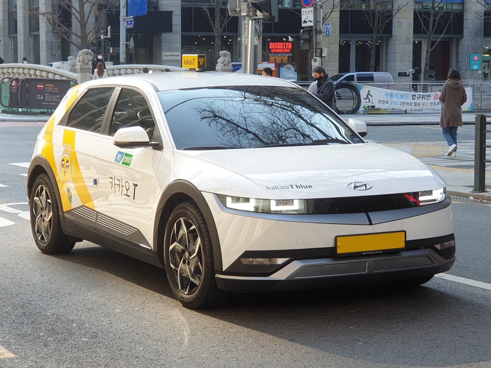 A white Kakao T Blue taxi with a yellow roof sign on a street in Seoul