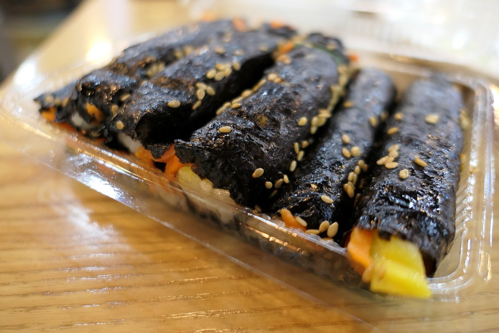 Small seaweed rice rolls topped with sesame seeds in a clear takeout tray