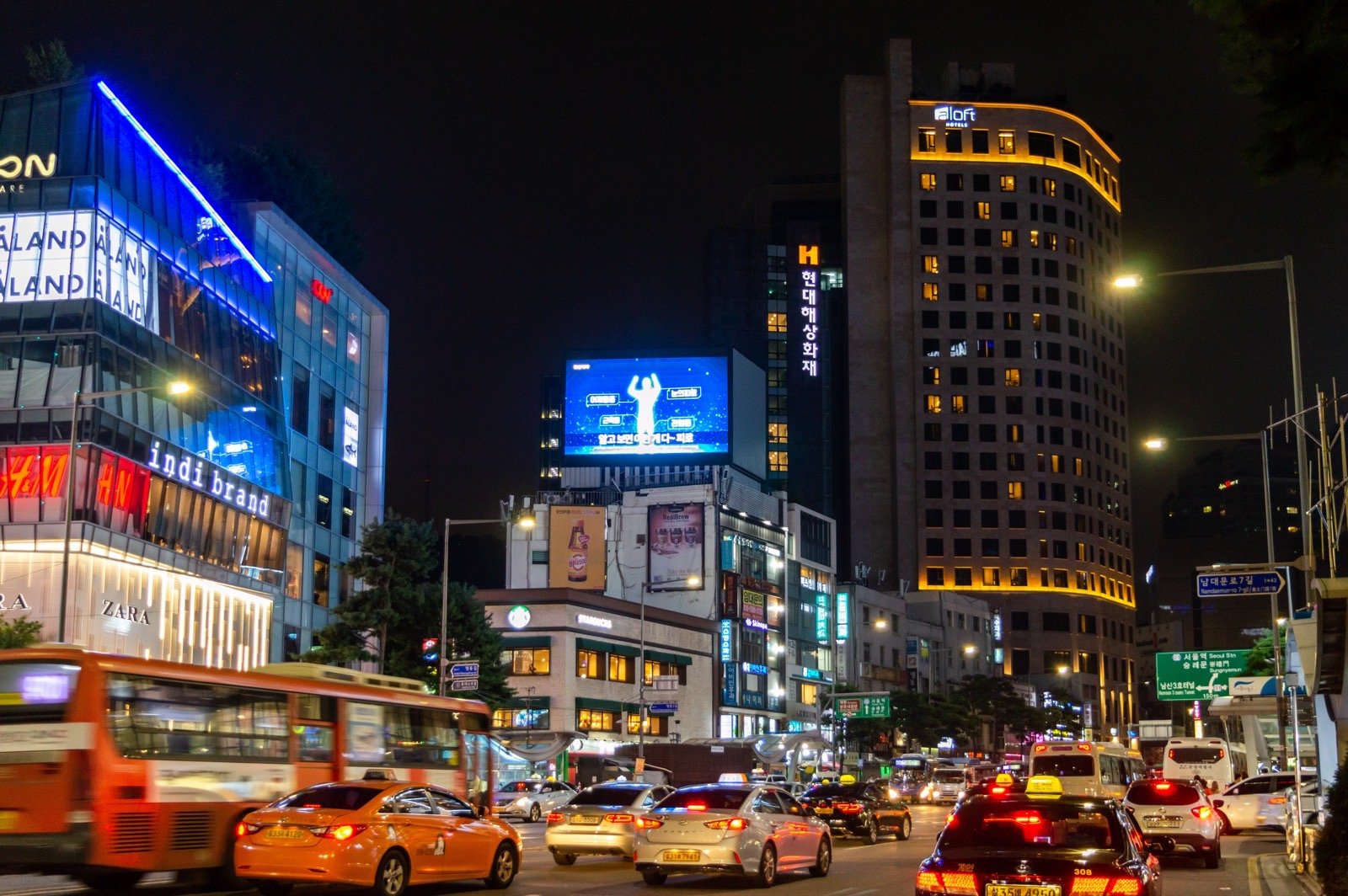Orange and white taxis and a city bus on Namdaemun-ro in Myeongdong, Seoul, at night