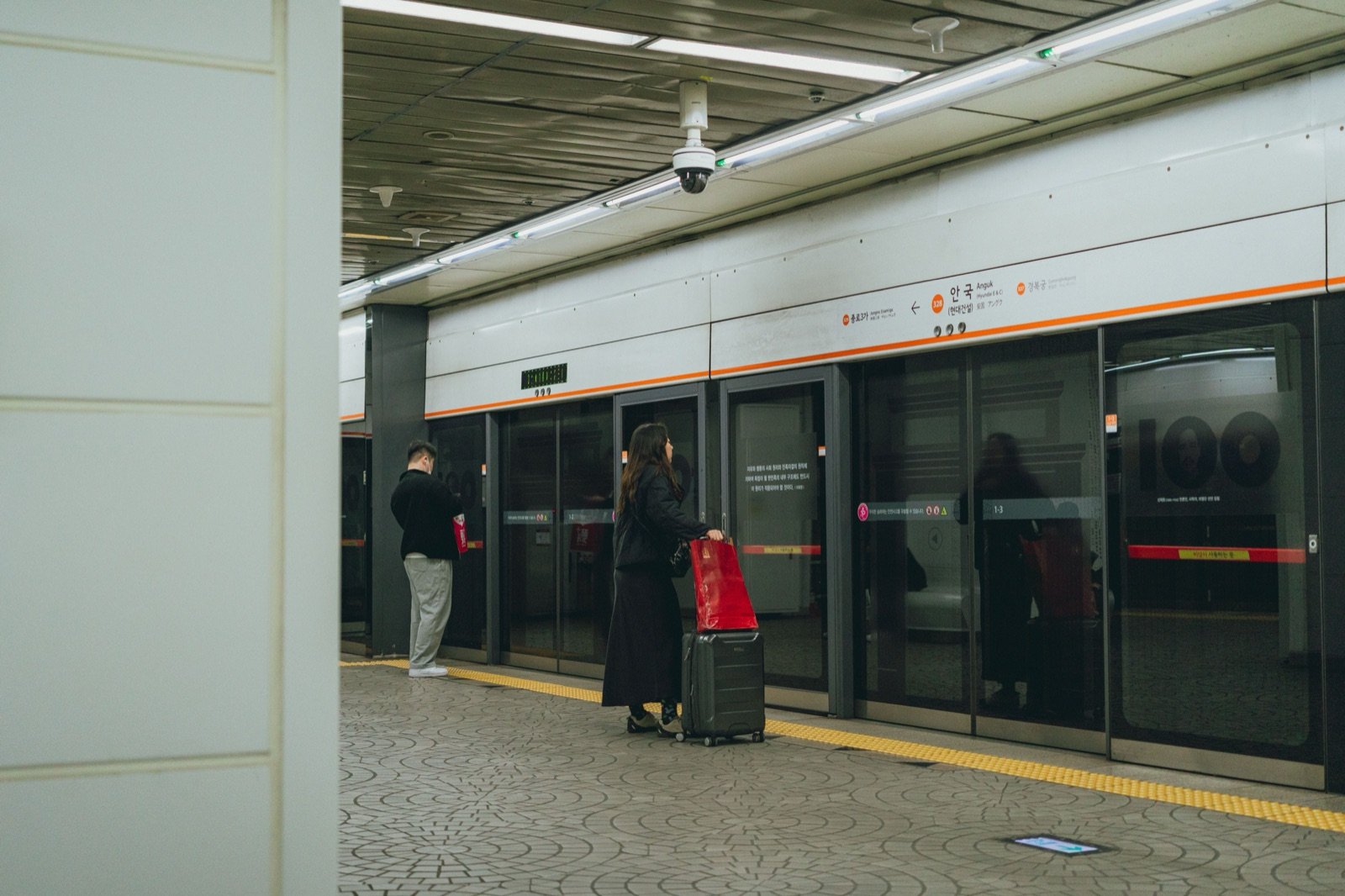Travelers with a suitcase waiting at the platform screen doors of Anguk Station on Line 3