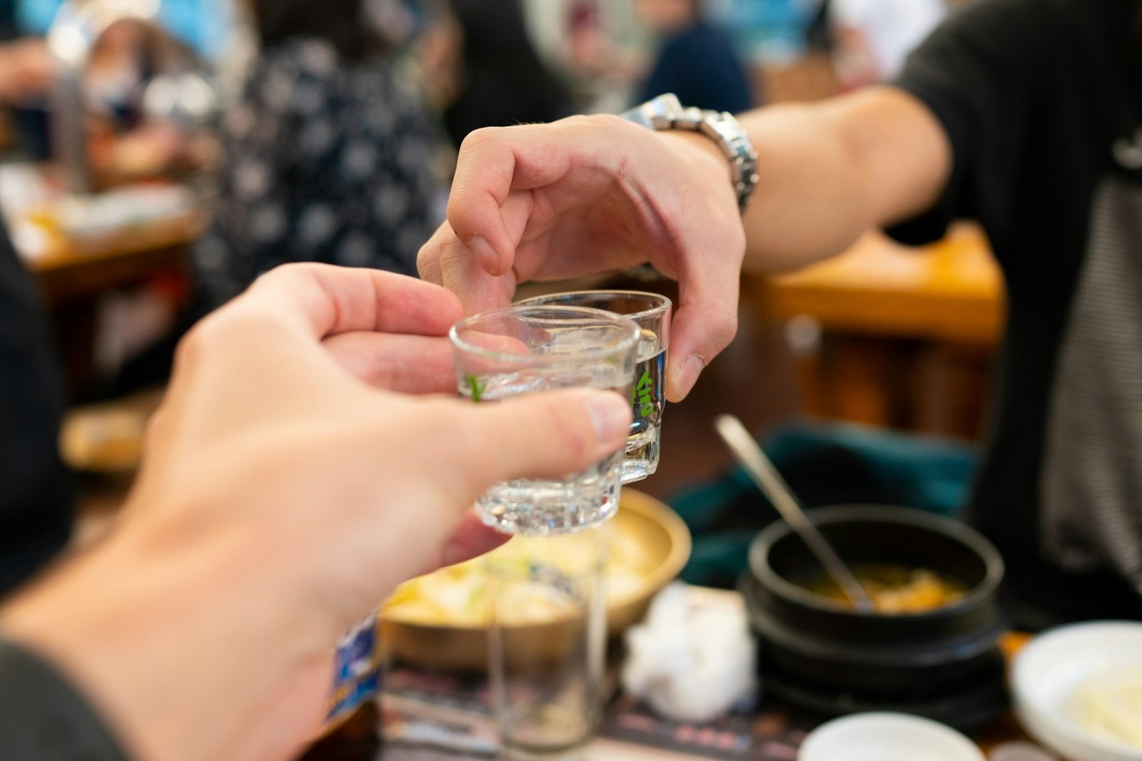 Two hands clinking small soju glasses over a restaurant table in Seoul